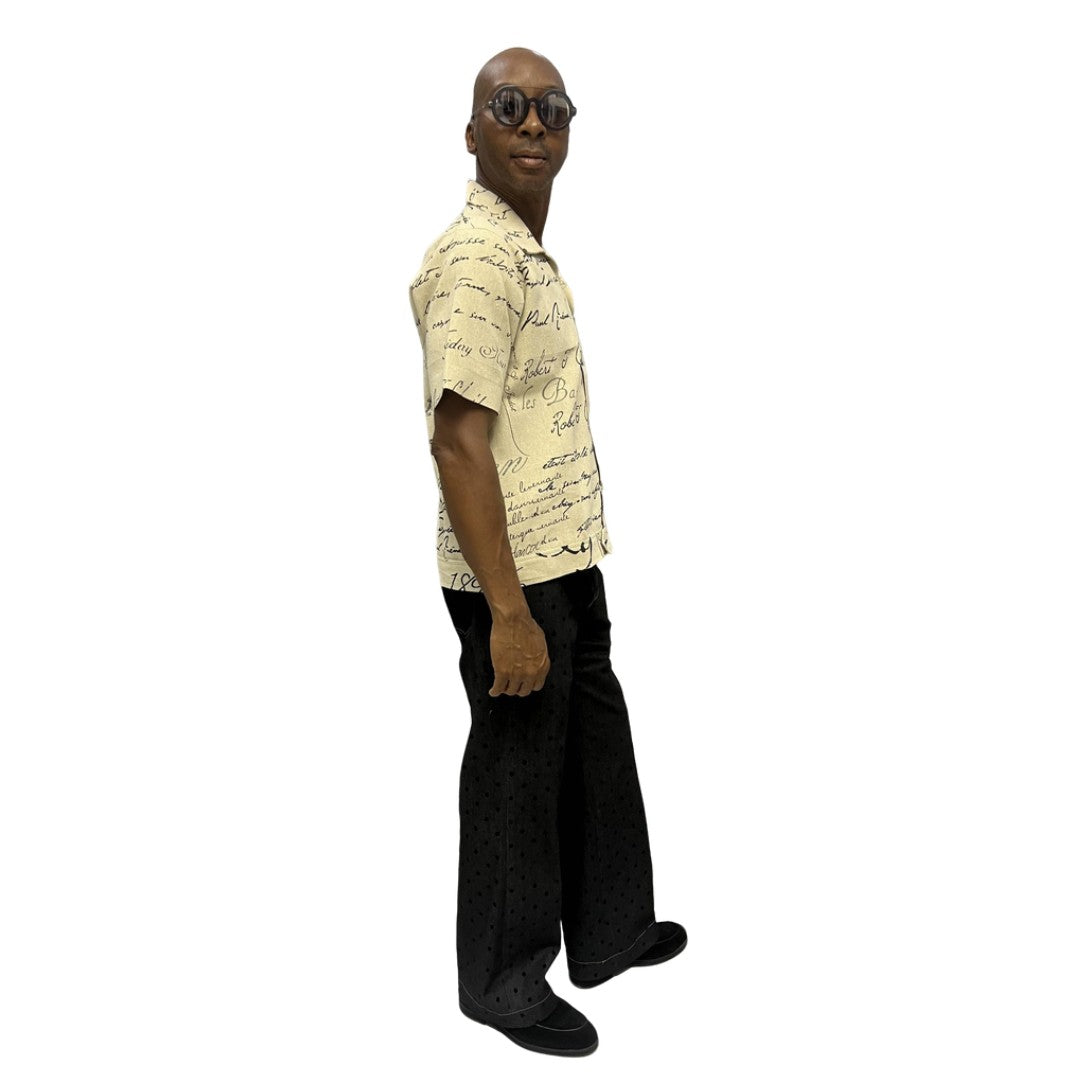 Short-sleeve cotton shirt featuring a black cursive script pattern on a cream-colored fabric with a button-down front and camp collar.