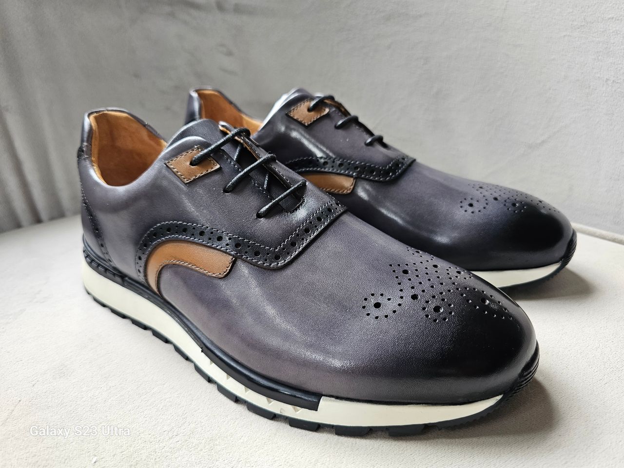 The Hybrid Derby featuring image_ae5dc9.jpg showing a slate-grey and tan leather upper, wingtip-style brogue perforations, and a white athletic outsole.