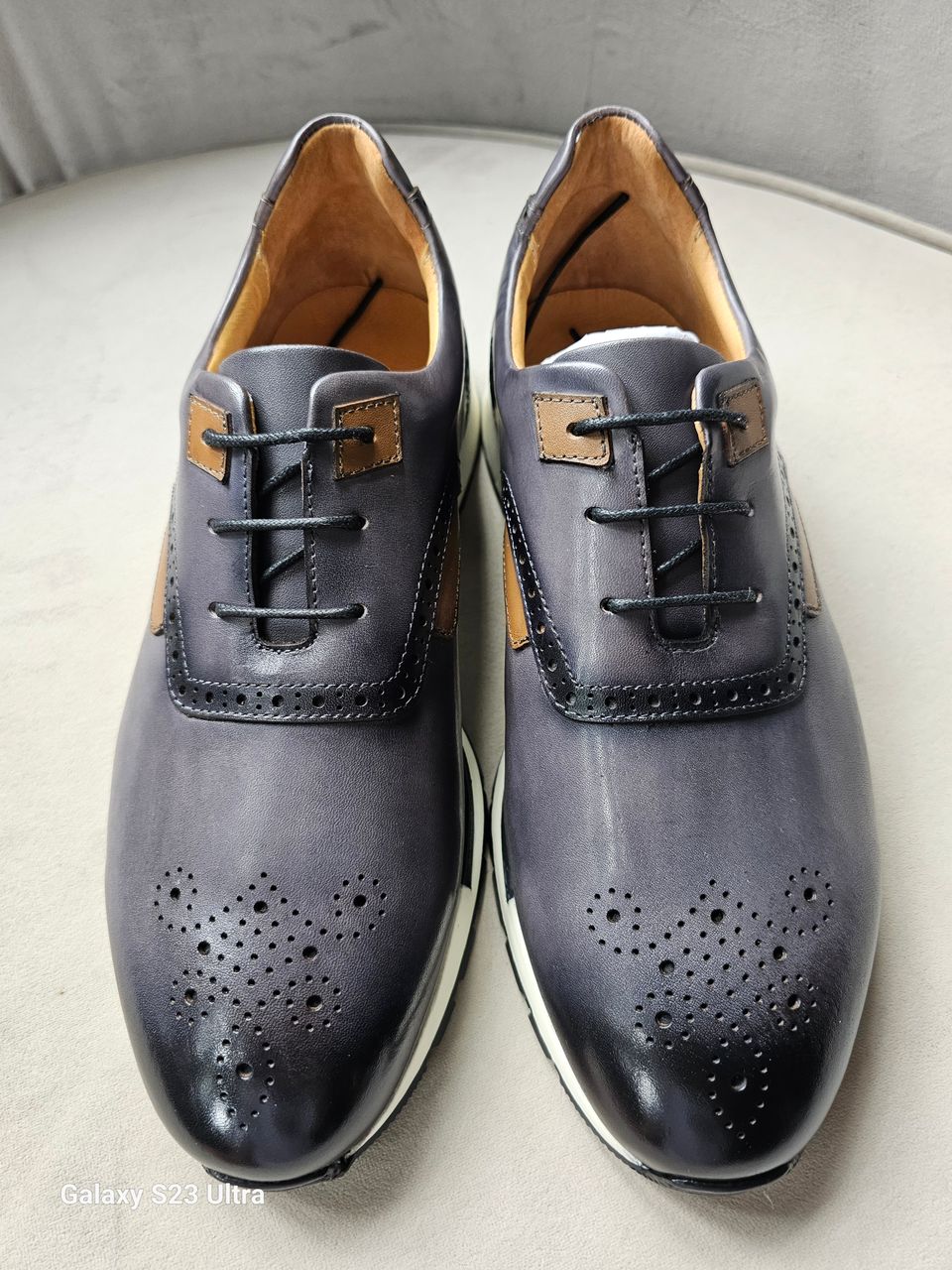 The Hybrid Derby featuring image_ae5dc9.jpg showing a slate-grey and tan leather upper, wingtip-style brogue perforations, and a white athletic outsole.