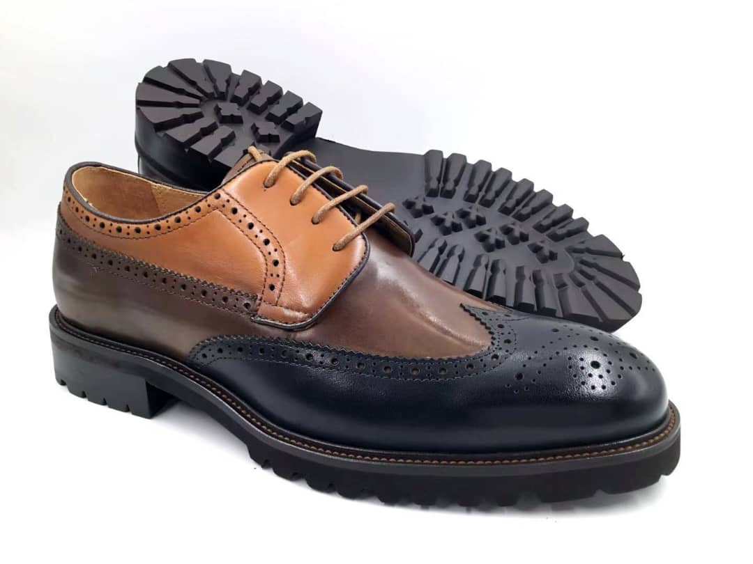 The Meridian Brogue Wingtip with its tri-tone navy, walnut, and tan leather upper, traditional brogue perforations, and a heavy-duty black lugged sole.