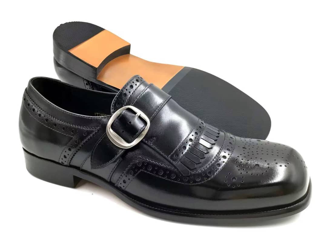 Modern Monk Strap with its polished black leather, decorative kiltie fringe, extensive brogue perforations, and a single silver-toned buckle.