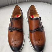 Double Monk Strap shoe featuring a hand-burnished tan leather upper with etched calligraphy, traditional medallion perforation on a rounded toe, and a contrasting white athletic sole.