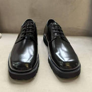 The Titan Lug Derby with its high-shine polished black leather, distinctive square-toe shape, and a thick, heavy-duty black lug sole.