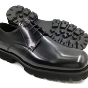The Titan Lug Derby with its high-shine polished black leather, distinctive square-toe shape, and a thick, heavy-duty black lug sole.