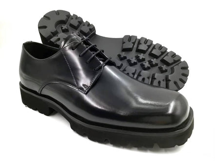 The Titan Lug Derby with its high-shine polished black leather, distinctive square-toe shape, and a thick, heavy-duty black lug sole.