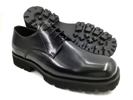 The Titan Lug Derby with its high-shine polished black leather, distinctive square-toe shape, and a thick, heavy-duty black lug sole.