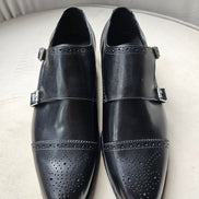The Zaki Monk with its polished black leather finish, intricate brogue detailing on the cap toe, and signature dual buckle closures.