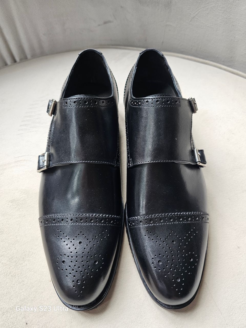 The Zaki Monk with its polished black leather finish, intricate brogue detailing on the cap toe, and signature dual buckle closures.