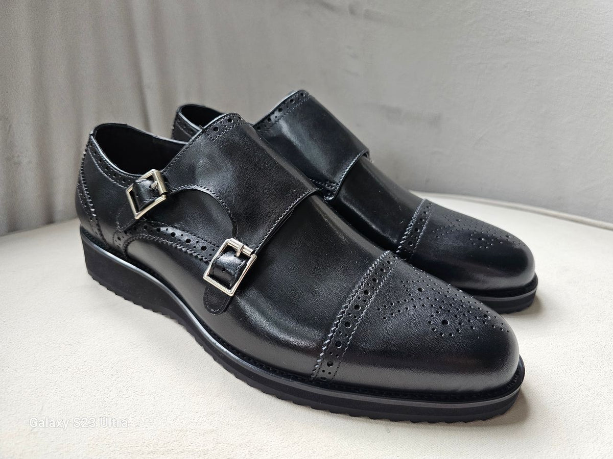 The Zaki Monk with its polished black leather finish, intricate brogue detailing on the cap toe, and signature dual buckle closures.