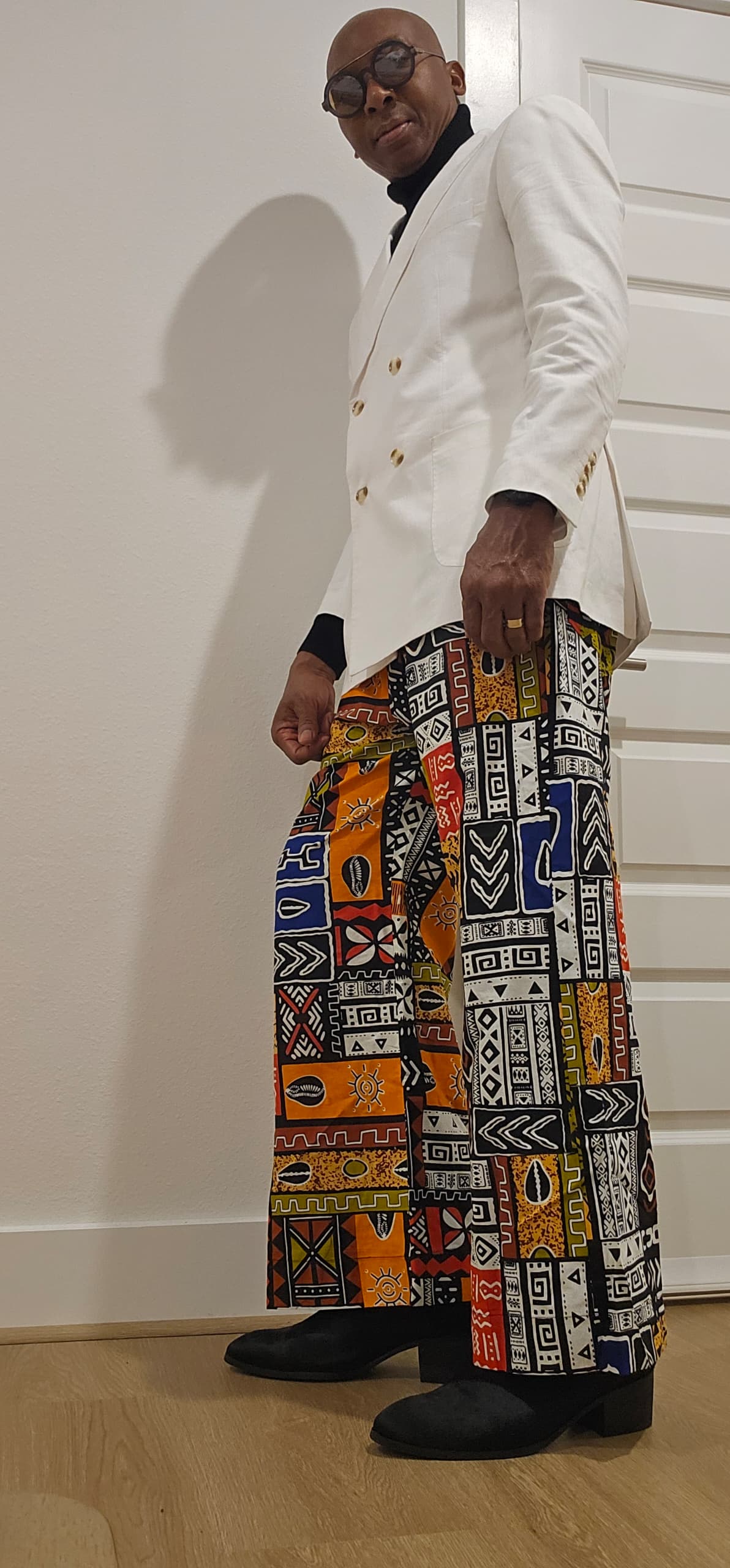 Trousers featuring a vibrant, multi-colored patchwork Ankara print with geometric and tribal motifs in a dramatic wide-leg silhouette.