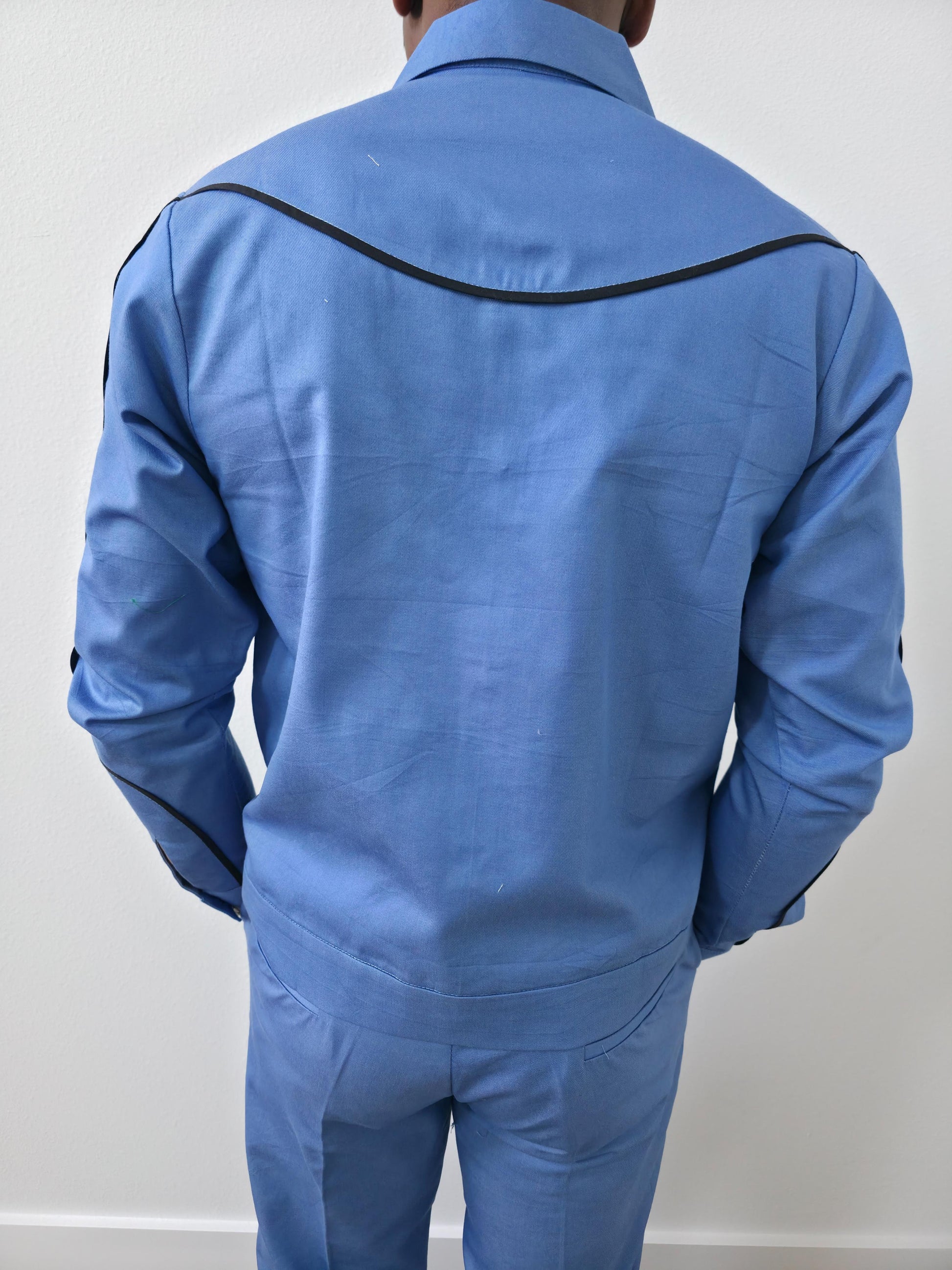 Azure blue two-piece set featuring a long-sleeved cowboy-style jacket with black western piping and matching tailored trousers. -Back View