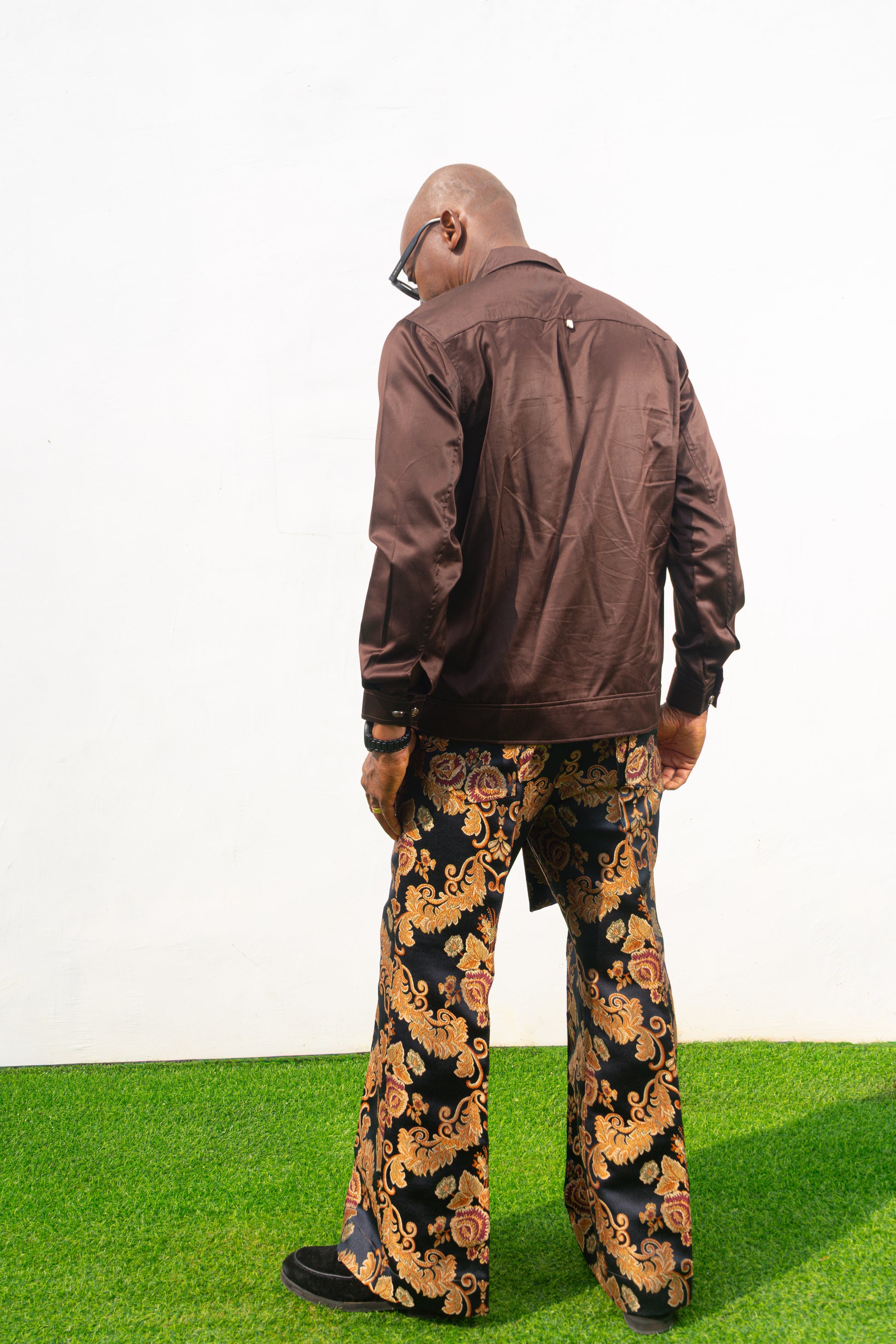 Two-Piece Set   featuring a chocolate brown long-sleeve button-down shirt with metallic hardware and ornate gold and navy patterned palazzo trousers.
Back Posing 