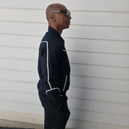 Two-piece black virgin wool suit featuring white contrast piping on the jacket chest and sleeves with matching tailored trousers.