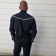 Two-piece black virgin wool suit featuring white contrast piping on the jacket chest and sleeves with matching tailored trousers.