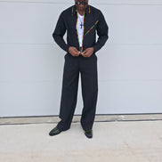 Two-Piece Set featuring a black virgin wool cropped zip-up jacket and wide-leg trousers accented by thin red, yellow, and green Ankara patterned piping.