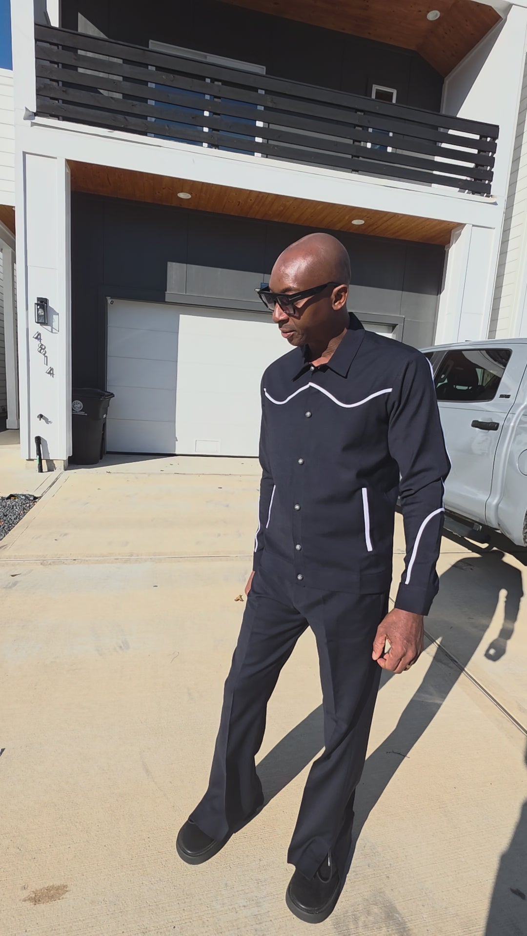 Two-piece black virgin wool suit featuring white contrast piping on the jacket chest and sleeves with matching tailored trousers.